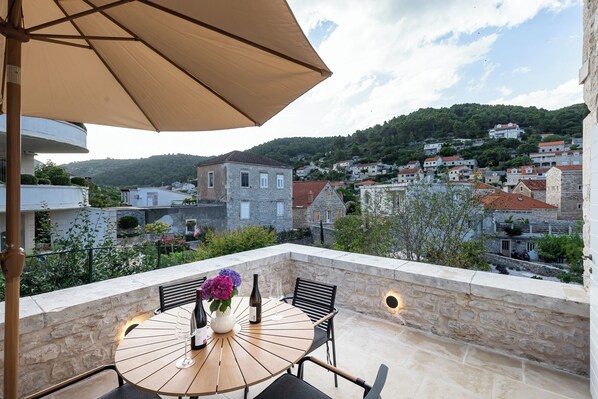 A terrace with a round table, two chairs, a vase with flowers, and a bottle of wine.