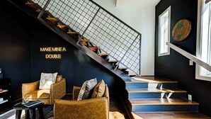 Eine Treppe mit Metallgeländer, eine schwarze Wand mit einem Neonlicht und eine Sitzecke mit Ledersesseln und einem kleinen Tisch.