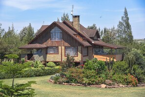 A rustic wooden house with a large front porch, a chimney, and a well-maintained garden with various plants and flowers.