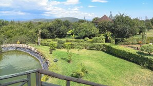 Un jardín ajardinado con un estanque, un edificio pequeño y vistas a colinas distantes.