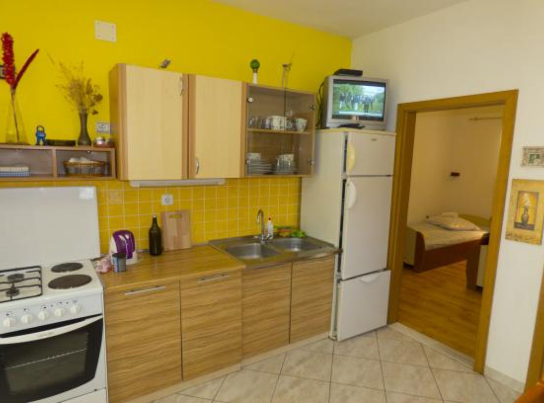 Una cocina compacta con armarios de madera, un refrigerador blanco, una estufa y un televisor pequeño.