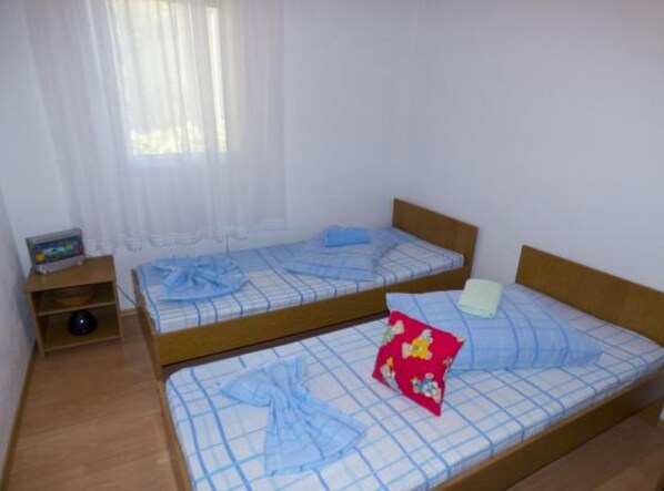 A room with two single beds, a small shelf with a toy, and a window with sheer curtains. - Beachfront Apartments Plaža (Jelsa)