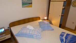 Een slaapkamer met een bed, nachtkastje, lamp, kledingkast en een schilderij aan de muur.