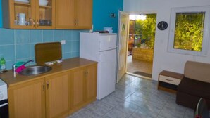 Een compacte keuken met houten kastjes, een koelkast en een gootsteen. Er is een klein zite hoekje met een tafel en stoelen. Een raam biedt uitzicht op de omgeving.