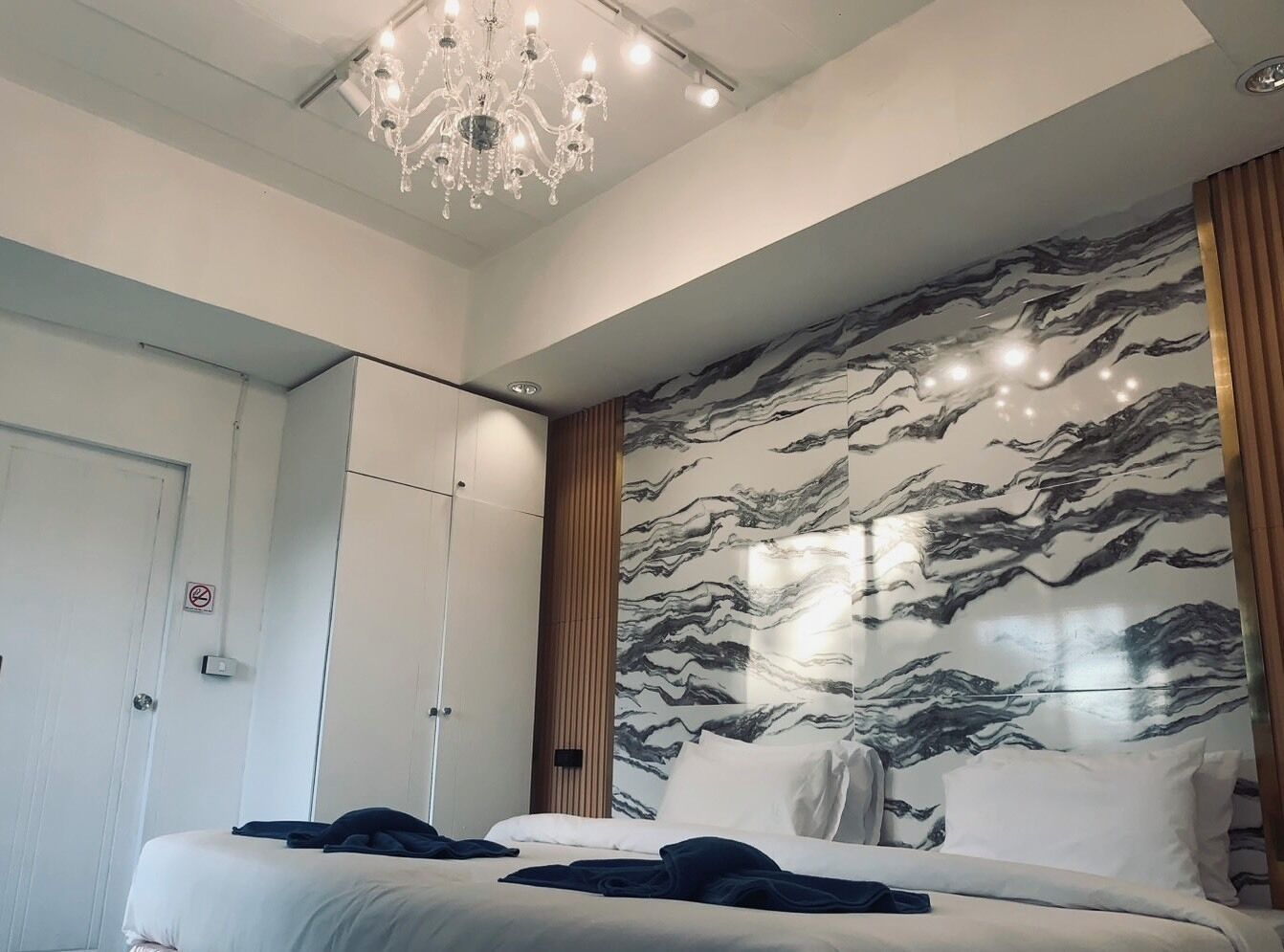 A modern bedroom with a large bed, a chandelier, and a marble-patterned wall.