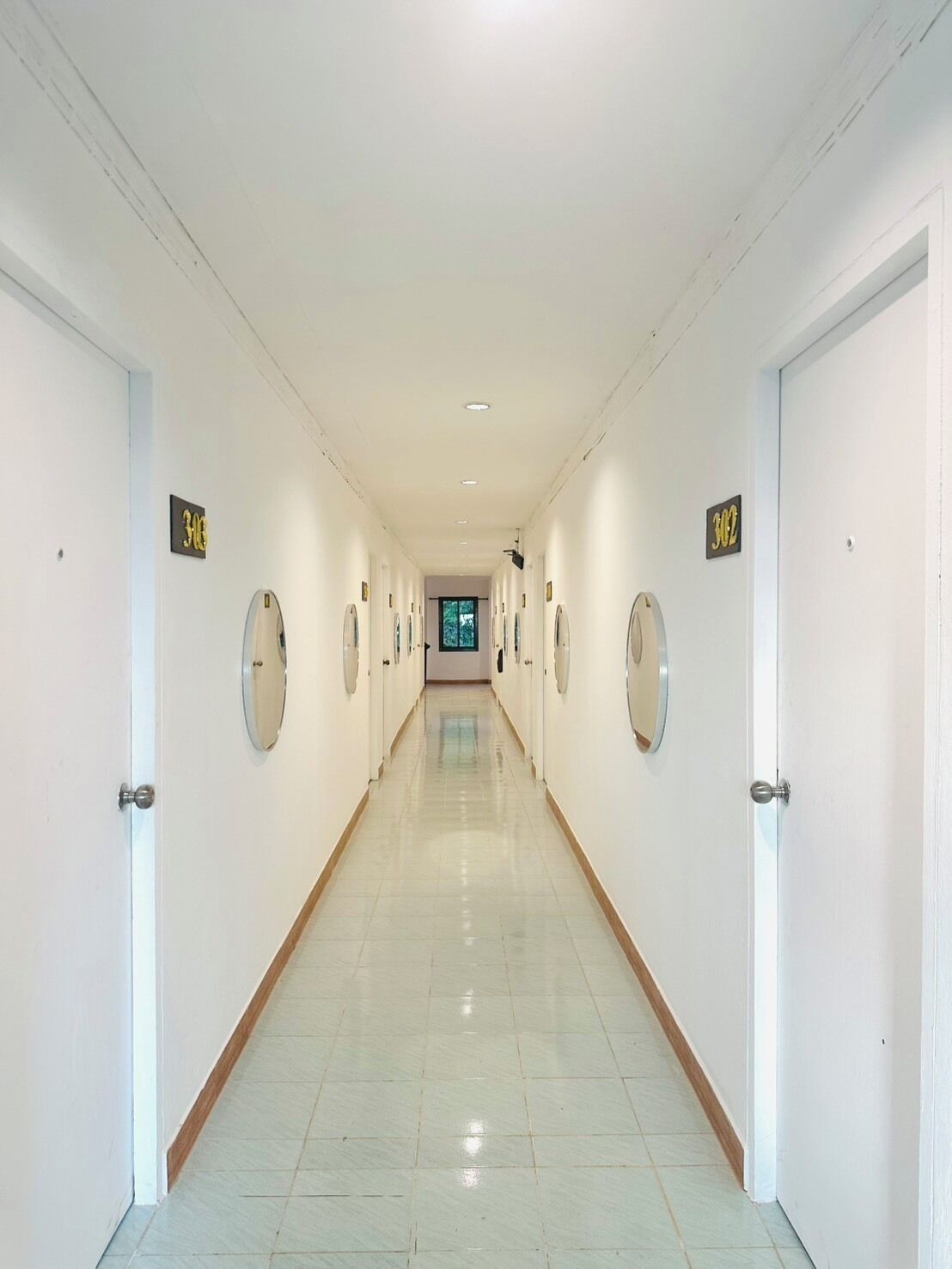 A long, well-lit hallway with doors on both sides, each marked with a number sign.