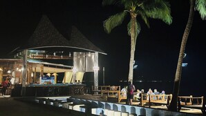 Un bar sulla spiaggia con una zona coperta, palme e una piscina.