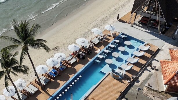 Area piscina con lettini e ombrelloni, una lunga piscina e una spiaggia sullo sfondo.