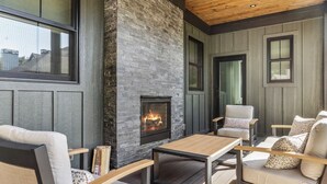A cozy outdoor seating area with a fireplace, wooden furniture, and a view of the surrounding neighborhood. - Serenity Now: Grand Beach Retreat, Heated Spa Pool, Hot Tub, Sauna, Golf Cart (New Buffalo)