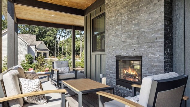 An outdoor patio with a stone fireplace, seating, and a view of a house in the background. - Serenity Now: Grand Beach Retreat, Heated Spa Pool, Hot Tub, Sauna, Golf Cart (New Buffalo)