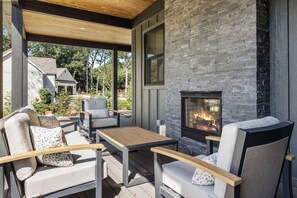An outdoor patio with a stone fireplace, seating, and a view of a house in the background. - Serenity Now: Grand Beach Retreat, Heated Spa Pool, Hot Tub, Sauna, Golf Cart (New Buffalo)