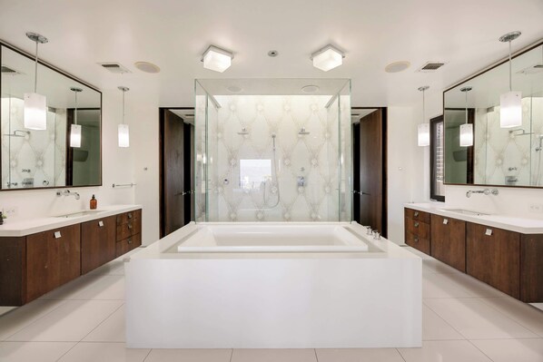 A modern bathroom with a large bathtub, two sinks, and mirrored walls.