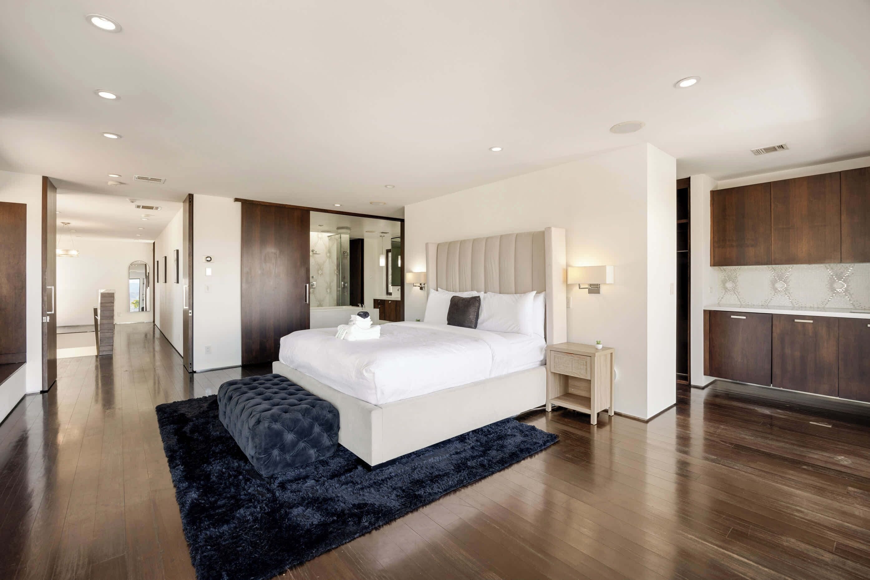 A modern bedroom with a large bed, bedside tables, a dark rug, and a wooden floor.