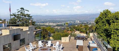 Una terraza en la azotea con mobiliario exterior, una chimenea y vistas a un paisaje urbano.