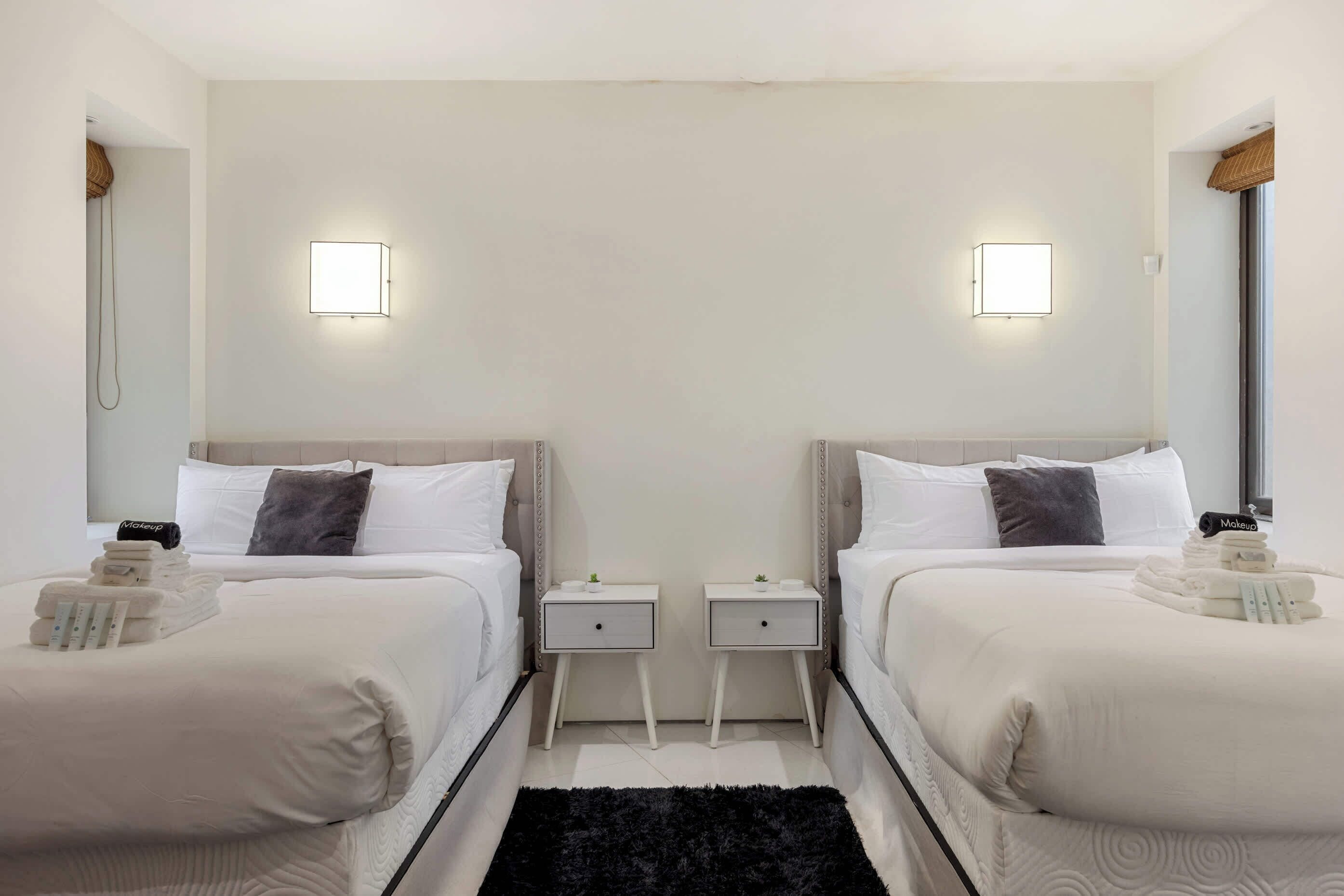 A hotel room with two beds, bedside tables, and wall-mounted lights.