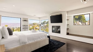 A modern bedroom with a large bed, a black rug, a TV, and a view of the outdoors.