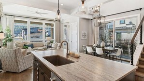 Un'ampia cucina con isola centrale, illuminazione a sospensione moderna e vista sull'esterno grazie a ampie finestre.