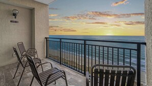 Een balkon met uitzicht op de oceaan bij zonsondergang, met een hekwerk, een stoel en een bord aan de muur.