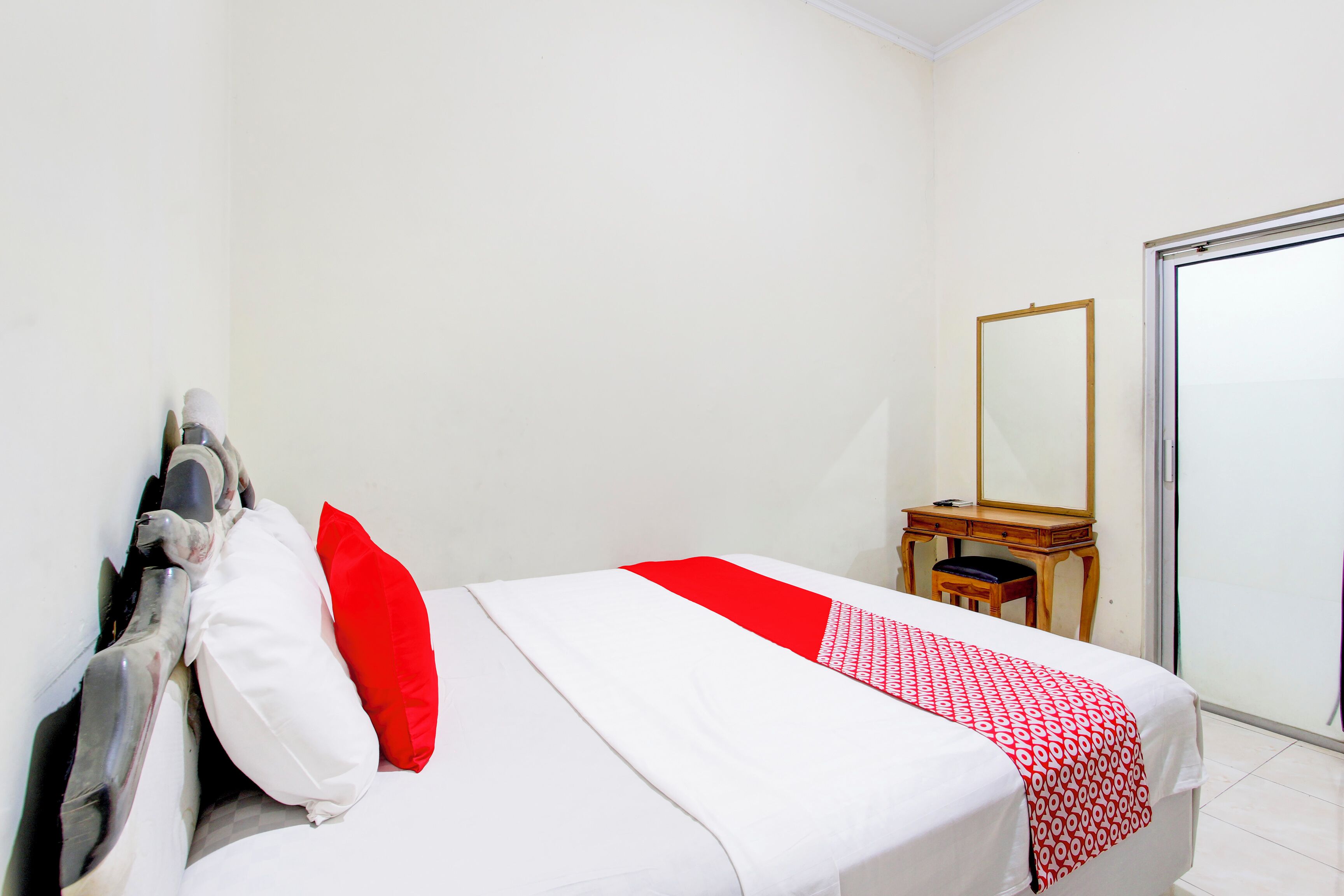Una habitación de hotel con cama, escritorio, silla, espejo y puerta corrediza.