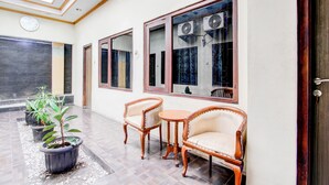 A spacious indoor area with a tiled floor, a skylight, and a large window with air conditioning units. There are three potted plants and two wooden chairs with cushions. - Hotel O Jalan Malioboro Near Stasiun Tugu Yogyakarta Formerly Hotel Baru (Yogyakarta)