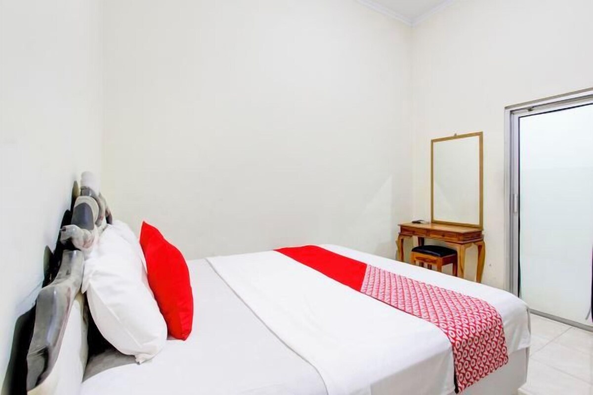 A hotel room with a bed, a mirror, a desk, and a sliding door.