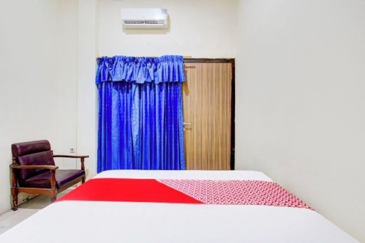 A room with a bed, a chair, a door with curtains, and an air conditioning unit.