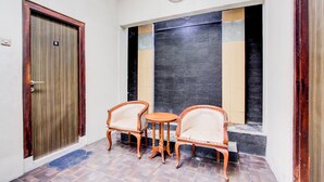 A room with a wooden door, a clock, two chairs, a small table, and a patterned wall. - Hotel O Jalan Malioboro Near Stasiun Tugu Yogyakarta Formerly Hotel Baru (Yogyakarta)