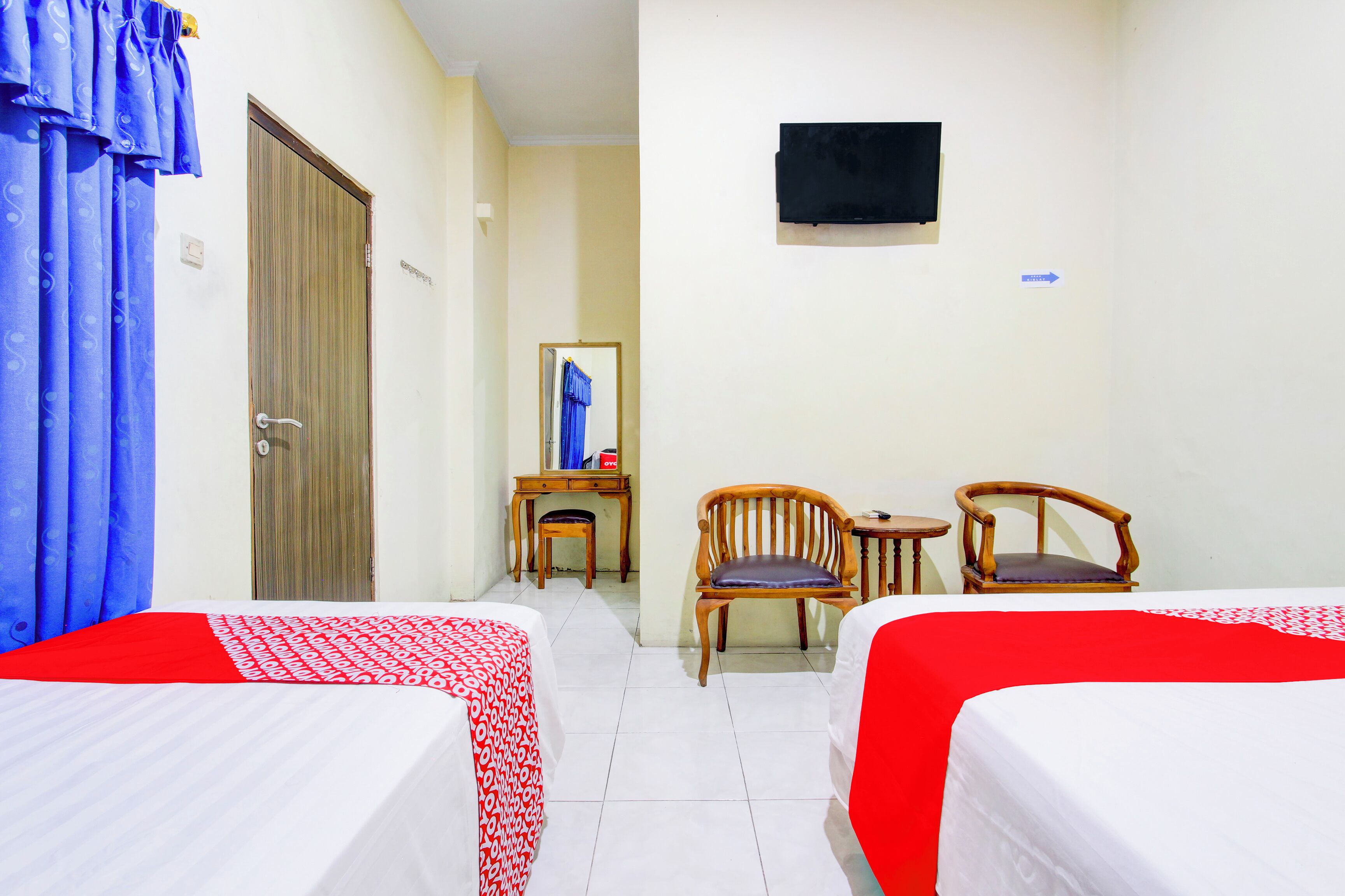 A hotel room with two beds, a desk, two chairs, a television, and a mirror.