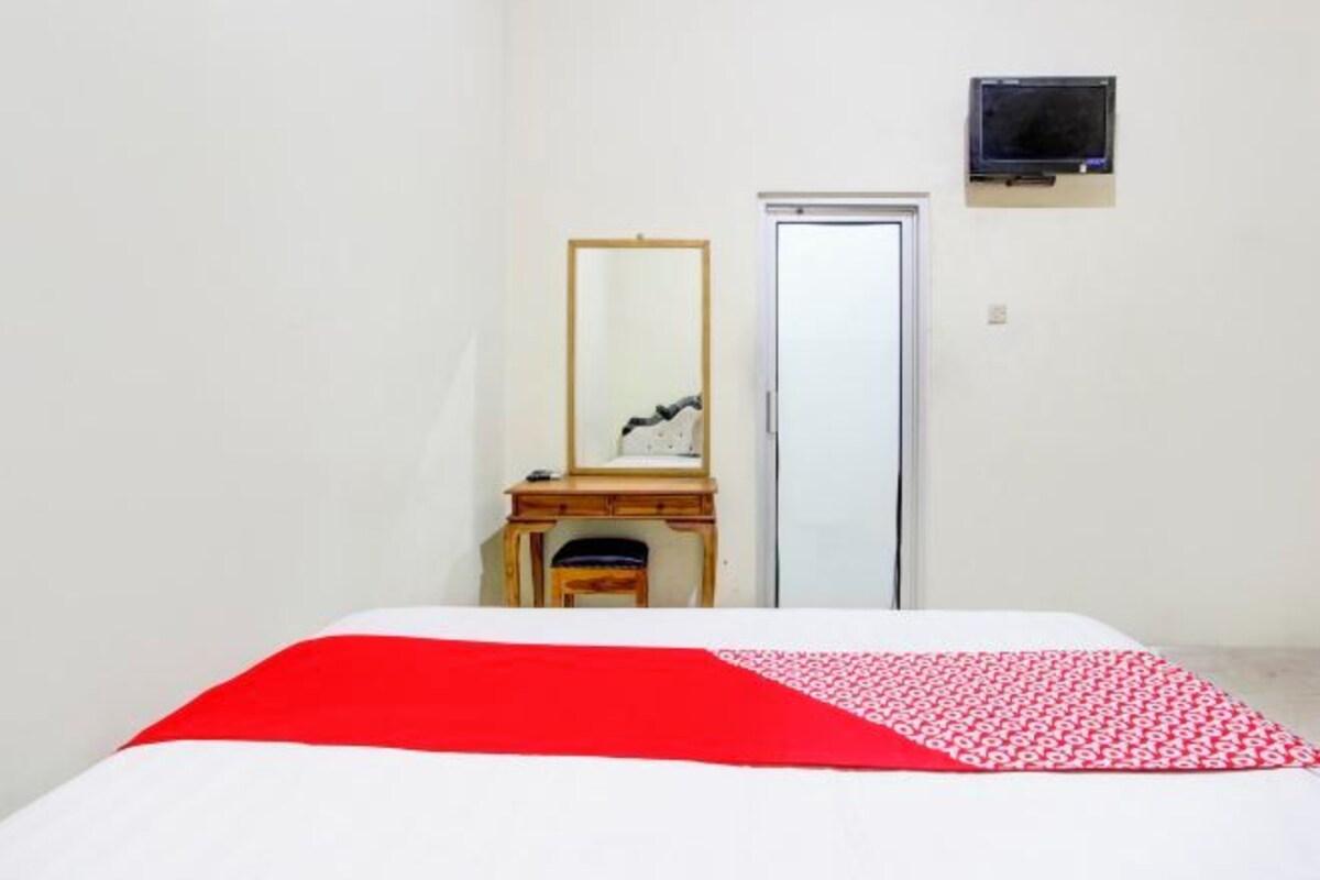 A room with a bed, a wooden dresser, a mirror, a door, and a television on the wall.