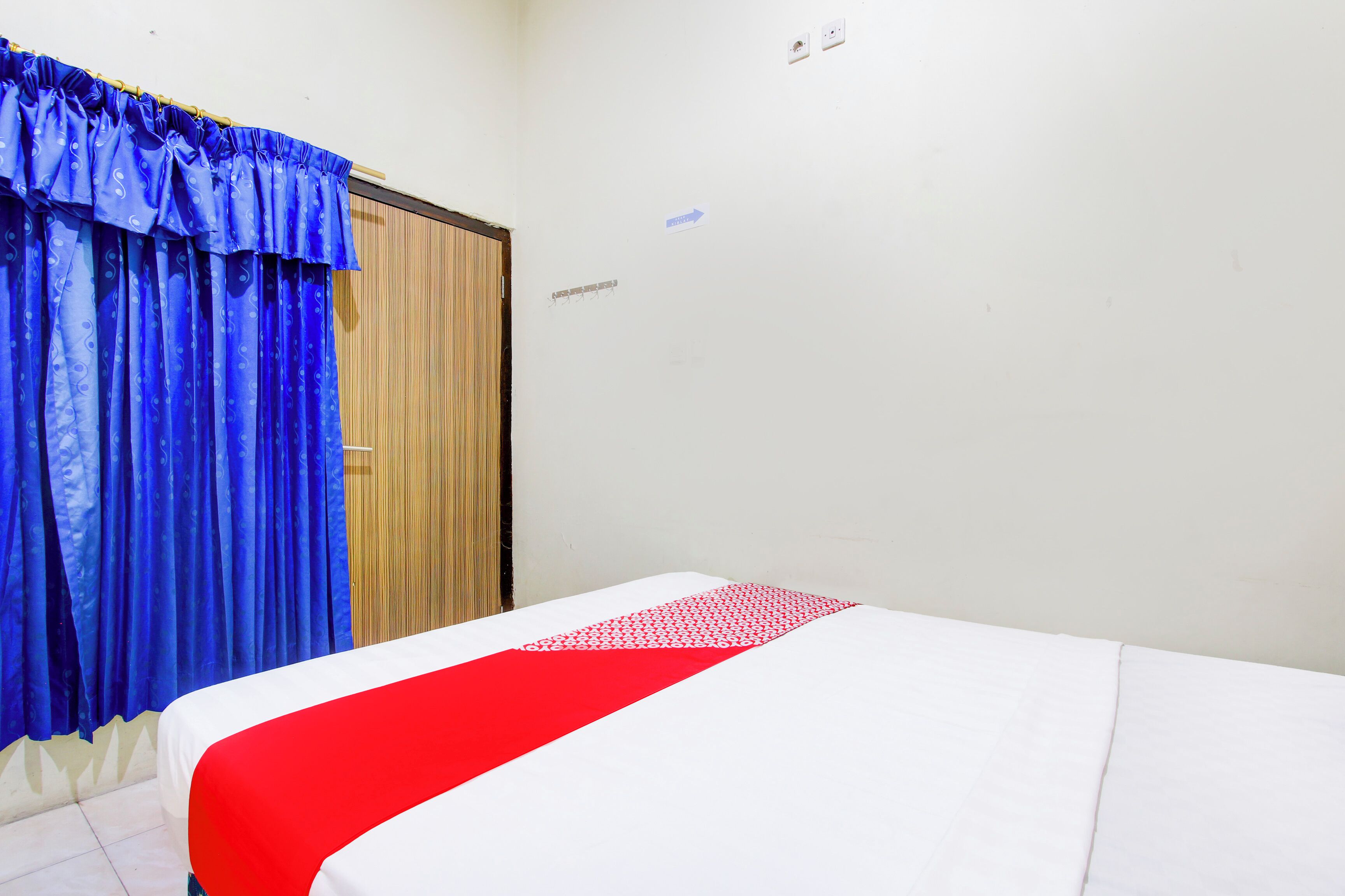 A room with a bed, blue curtains, a wooden door, and a white wall with a sign.