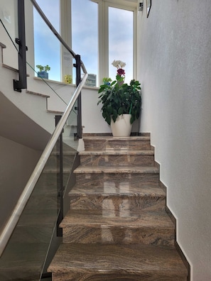 A modern staircase with a glass railing, leading to a landing with a potted plant. - Villa Analena (Sibenik)