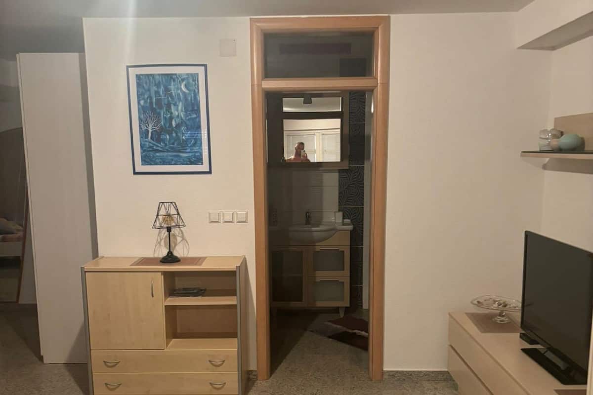 Ein Zimmer mit einem Holztisch, einem Fernseher, einem Spiegel und einem Kleiderschrank.