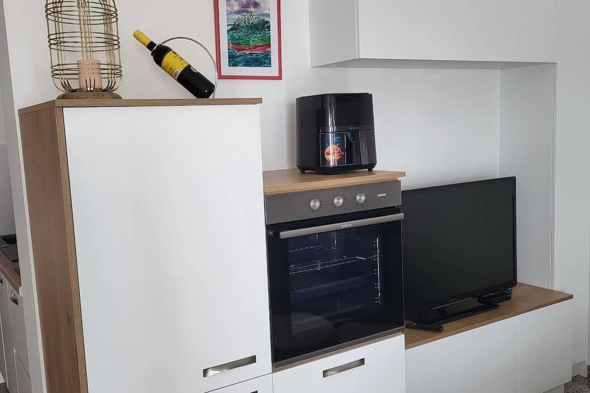 Eine moderne Küche mit Backofen, einem Fernseher auf einer Holzablage und einer Weinflasche auf der Arbeitsplatte.