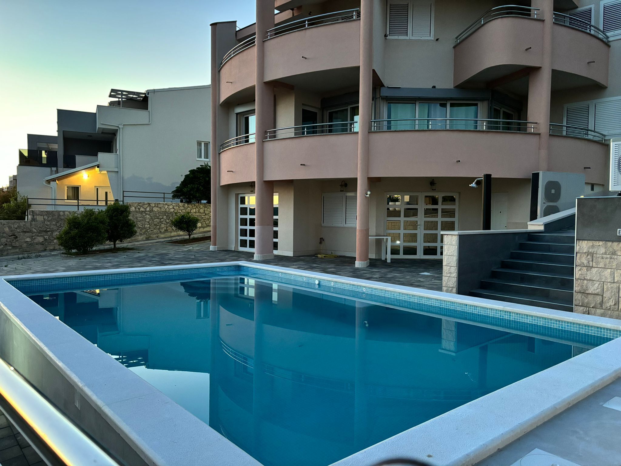 A modern building with a swimming pool, balconies, and a stone wall.