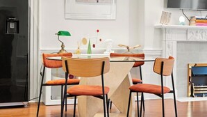 Una cocina moderna con un refrigerador negro, una mesa de comedor con cuatro sillas naranjas y una pared blanca con un cuadro enmarcadosobre la chimenea.