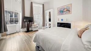 Un dormitorio con una cama grande, una chimenea, un televisor y un ventanal con cortinas.