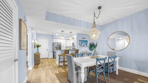 A dining area with a white table and blue chairs, a chandelier, and a round mirror on the wall. - RIVER FLY IN: Sunshine Suite, Waterfront 2BR (Merritt Island)