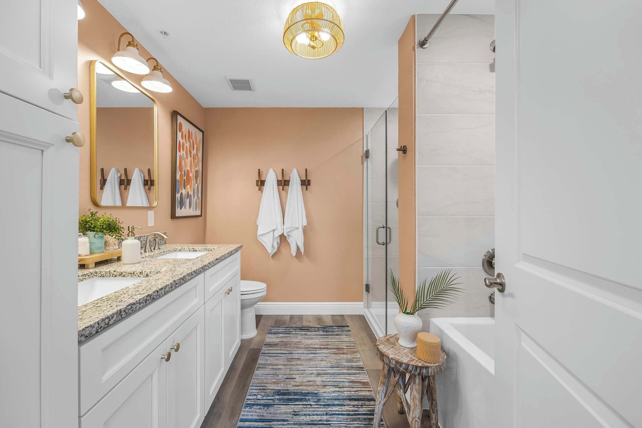 A bathroom with a vanity, sink, mirror, towel rack, shower, and a small round table with a plant.