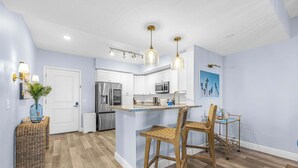 A modern kitchen with white cabinets, stainless steel appliances, and a central island with bar stools. - RIVER FLY IN: Sunshine Suite, Waterfront 2BR (Merritt Island)