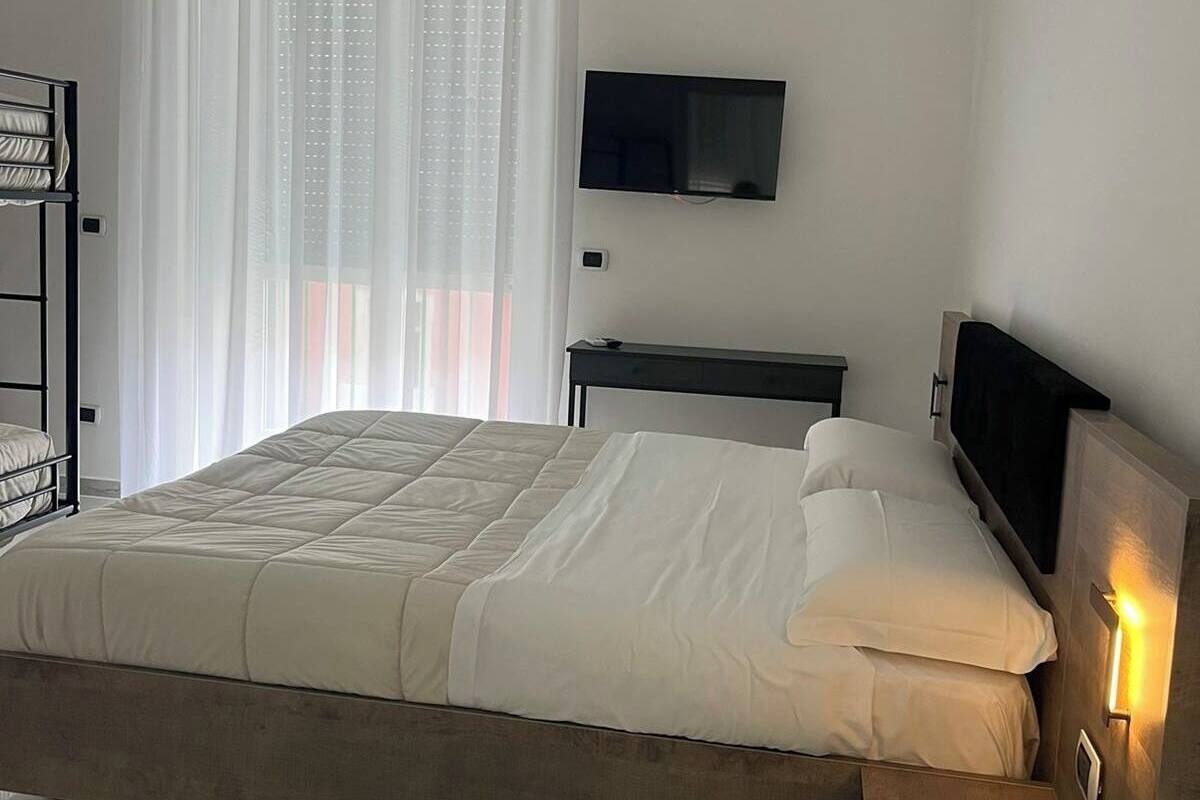 A neatly arranged bedroom with a bed, a TV mounted on the wall, and a window with sheer curtains.