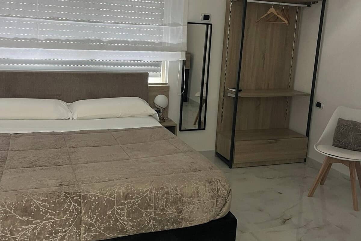 A bedroom with a bed, a wardrobe, a chair, and a bedside table.