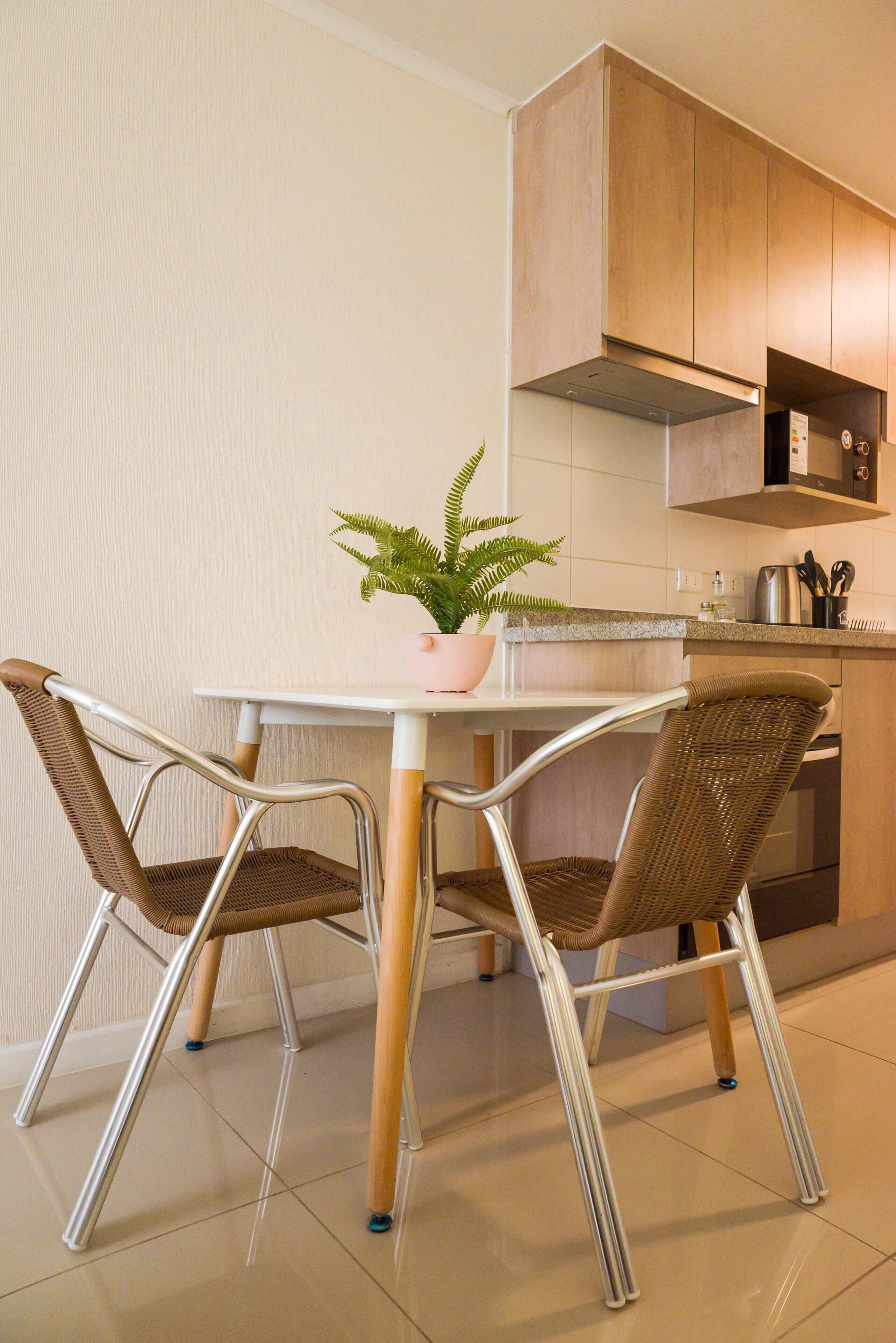 Eine moderne Küche mit einem weißen Tisch, zwei Korbstühlen, einem Blumentopf und Holzschränken.