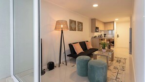 A modern apartment with a living area featuring a sofa, a coffee table, and a floor lamp. A kitchen is visible in the background with cabinets and a refrigerator. - Urban apartment Santa Rosa Ideal for Couples (Santiago)