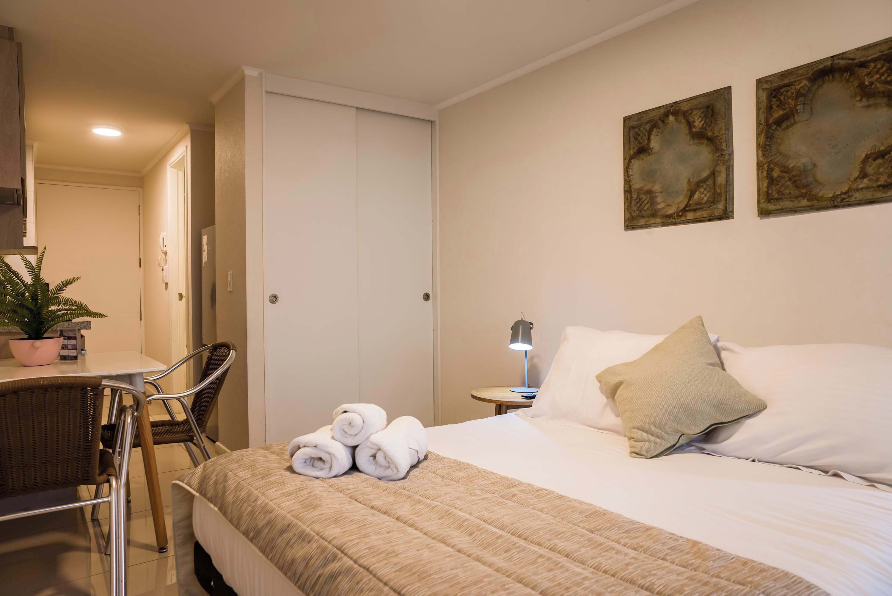 Une chambre d’hôtel avec un lit, une chaise, une table, une plante en pot et des œuvres d’art accrochées au mur.