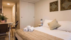 Habitación de hotel con cama, una silla, una mesa, planta en maceta y cuadros en la pared.