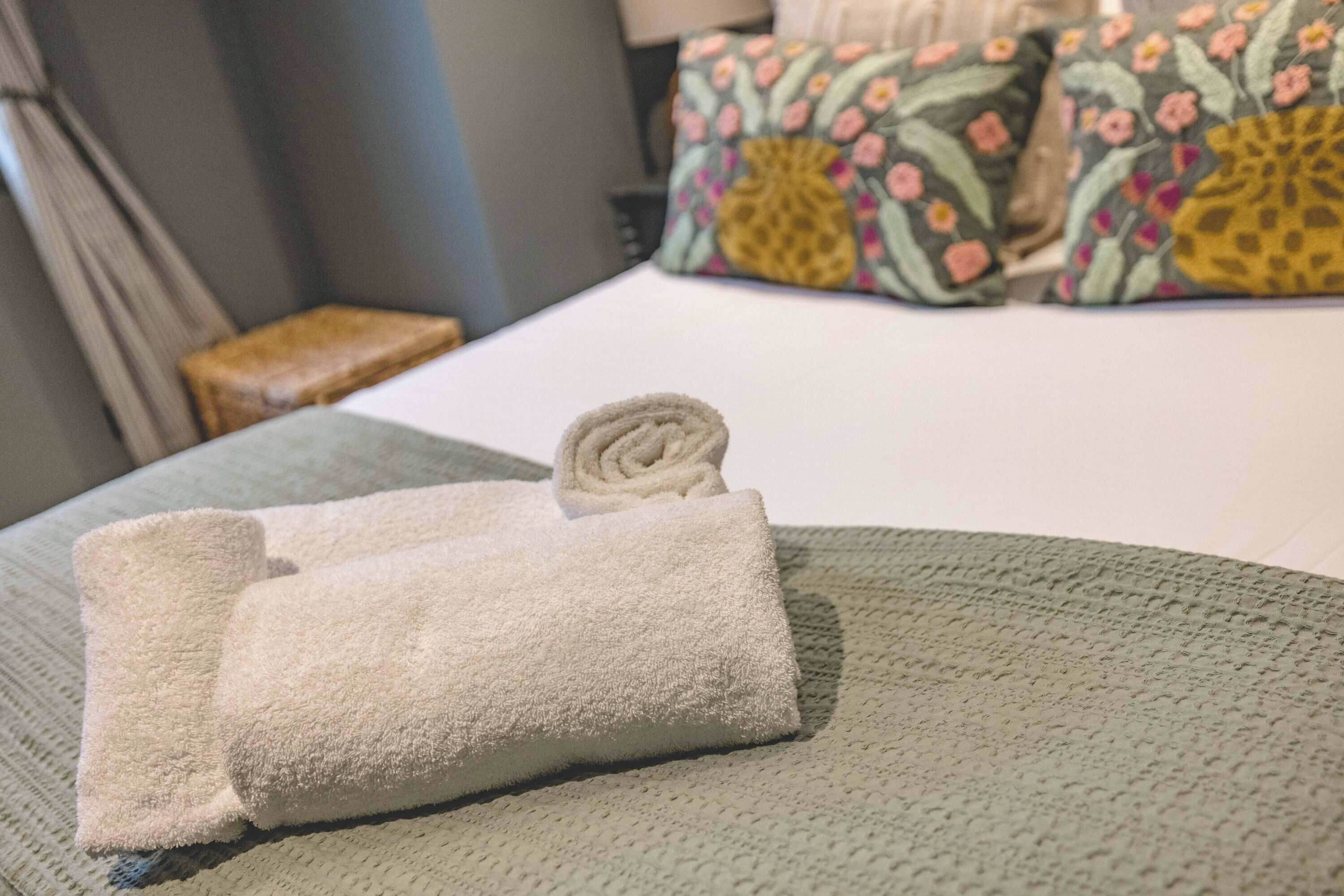 En prydligt vikt, vit handduk ligger på ett grönt, mönstrat överkast i ett hotellrum.