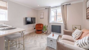 A modern living room with a sofa, a dining table with chairs, a TV, and a window with curtains.