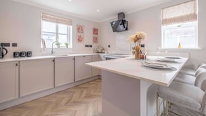 A modern kitchen with white cabinets, a central island, a flat-screen TV, and decorative wall art.