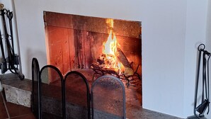 Una chimenea con fuego, un espejo encima y dos macetas sobre la repisa.