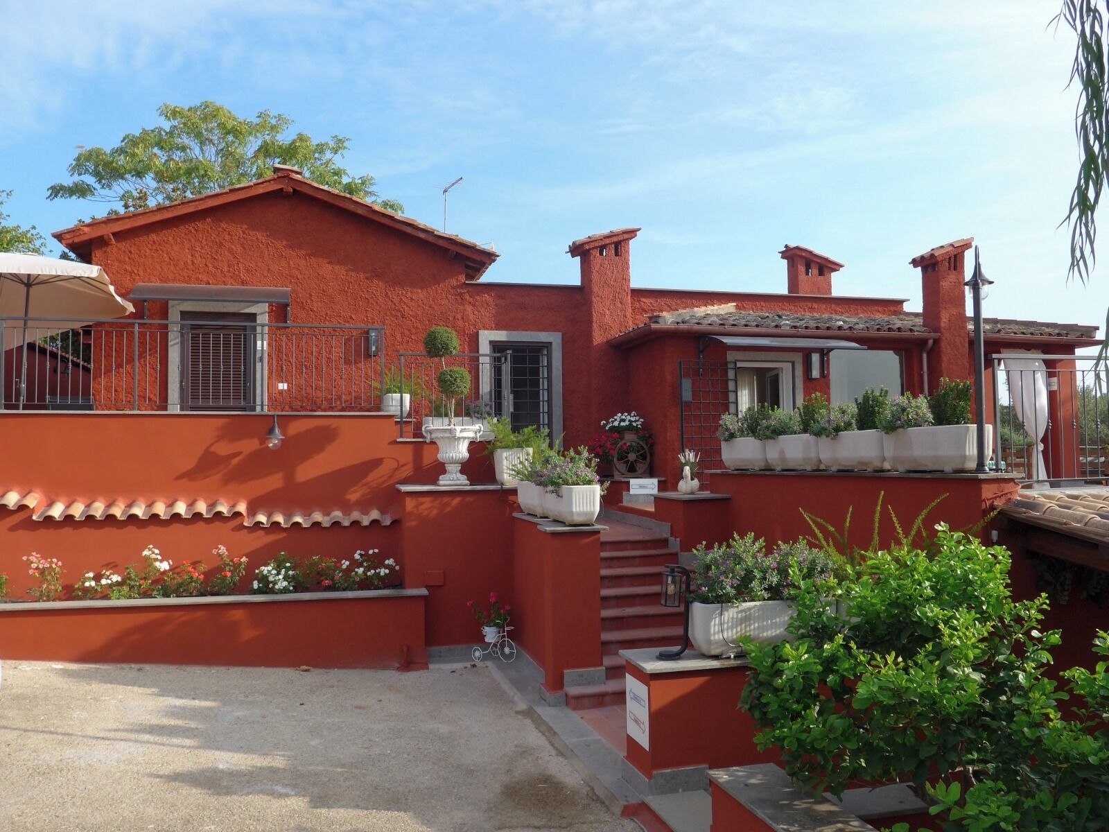 Una casa de revoque rojo con tejado de tejas, un pequeño porche con plantas en macetas y una escalera que lleva a la entrada.